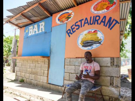 Tyron Wilson sits in front of his food shop near the Caymanas River on Tuesday, May 4. COVID-19 protocols have caused a lockdown of dozens of rivers and beaches across Jamaica.