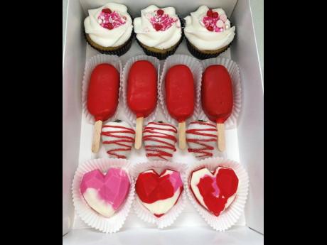 A mixed box of sweet treats, including cupcakes, cakesicles, chocolate-covered strawberries and breakable hearts.