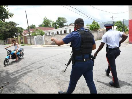 Policemen beckon to a motorcyclist to stop near a state-of-emergency checkpoint in central Kingston on Sunday, June 14, 2020.
