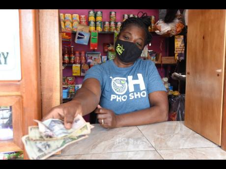 Michelle Swearing, shopkeeper at Top Road in Mavis Bank, hands change to a customer on the weekend. She says that transportation costs linked to the Gordon Town road breakaway have had to be passed on to customers.