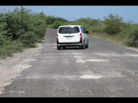 A motor car navigates its way in between potholes along a stretch of roadway in south-west Clarendon.