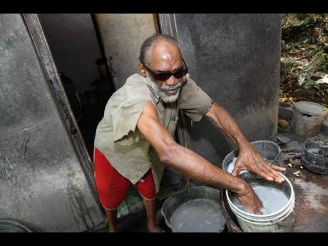 Beresford Dixon washes his hands in a bucket outside his house in Kintyre, St Andrew, on Thursday.