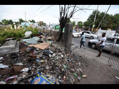 Commuters pass a mound of garbage at a ramshackle entrance of the No. 5 Cemetery in Spanish Town, St Catherine.