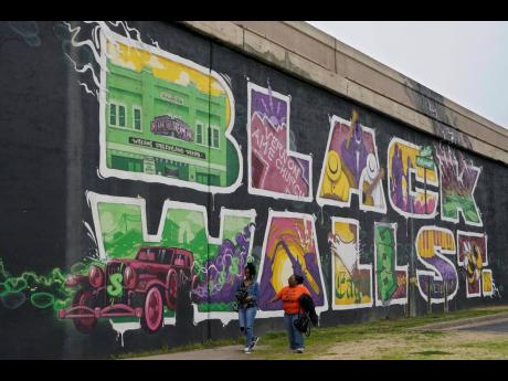 
Javohn Perry, left, of Seattle, and her cousin, Danielle Johnson, right, of Beggs, Oklahoma, walk past the Black Wall Street mural in Tulsa, Okla. The original Black Wall Street vaporised a hundred years ago, when a murderous white mob laid waste to what 