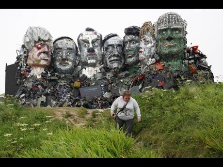 A visitor walks away from a sculpture created out of e-waste in the likeness of Mount Rushmore and the G7 leaders on a hill in Hayle, Cornwall, England.