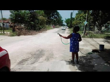 A resident sprays water on the exposed marl to lessen the dust nuisance along the recently paved roadway in Chantilly, Westmoreland, which was damaged less than a week after being handed over.