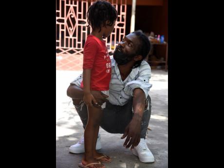 Kenrick Spencer stoops to talk to his three-year-old daughter, Tianna Spencer, at Oliver Gardens in May Pen, Clarendon, yesterday.