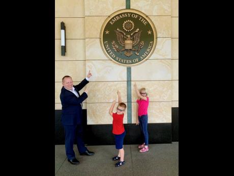 McIntyre tries to include his children in his diplomatic duties at the US Embassy. That way, they have a better understanding and will accept when daddy has to go off to work. From left: John McIntyre and children, Ian and Emma, point to the US Embassy’s