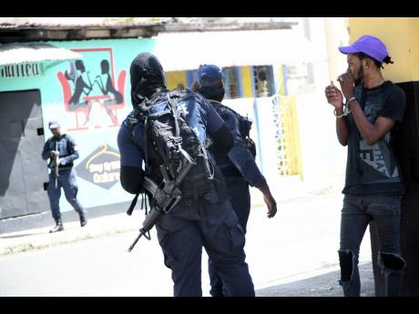 Police arrest a man while patrolling the streets of Arnett Gardens, south St Andrew, after a triple shooting in the community.