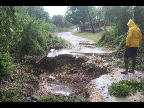 Denzil Hill of Gimme-Me-Bit surveys a collapsed road in the Clarendon community. He blamed the disaster on an unmaintained waterway.