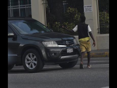 A street child rounds a motor vehicle at a popular begging spot on West Kings House Road in St Andrew on Wednesday. A CPFSA report found that intergenerational inequality and chronic poverty are among the factors that push youngsters on the road.  