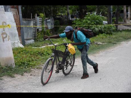 A man pushes his bicycle under a police tape used to cordon off an area where 19-year-old Kevon Morgan was shot and killed in Homestead, Spanish Town, St Catherine, on Thursday.
