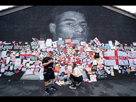A boy stands by messages of support left on a mural of Manchester United striker and England player Marcus Rashford, on the wall of the Coffee House Café on Copson Street in Withington, Manchester, England, on Tuesday. The mural was defaced with graffiti 