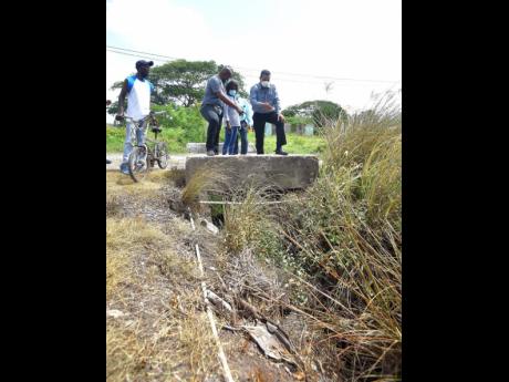 Minister of State in the Ministry of Local Government and Rural Development, Homer Davis (right), and Member of Parliament for South West Clarendon, Lothan Cousins (left), point to a blocked drain in the community of Banks during a tour on July 22. Looking