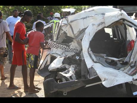 Two youngsters look intently inside a Toyota Probox motorcar that was involved in an accident along the Toll Gate main road in Clarendon yesterday. One man died as a result of the crash. Two persons are in critical condition in hospital.