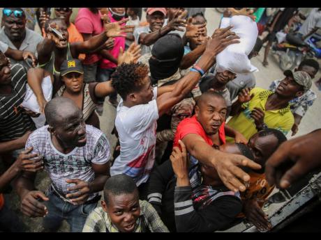 Earthquake victims scramble for handouts of rice at a food distribution site in Les Cayes, Haiti, on Monday. Haitians are searching for survivors and the dead in collapsed buildings following the powerful earthquake over the weekend.