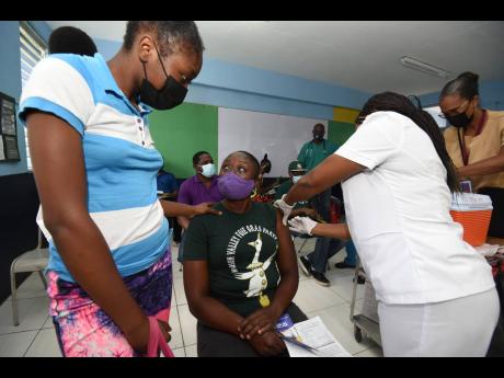Public health nurse Ugbojoide Obaje vaccinates Patricia Caine, a resident of St Andrew West Rural, during a vaccination blitz that was held at Stony Hill Technical High School on Thursday. Caine's daughter Sherinae Brown offered moral support because her m
