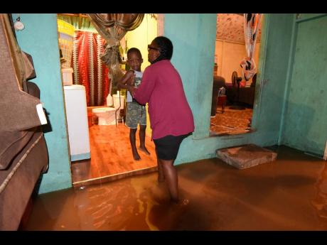 Latoya Campbell lifts her son to safety inside her home in Bannister, St Catherine, which was flooded during the passage of Tropical Storm Grace on Tuesday.