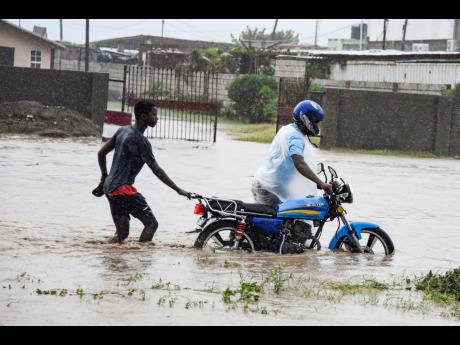 Two men push a disabled motorcycle through deep water in Seven Miles, Bull Bay, as flood rains lashed eastern Jamaica on Tuesday. 