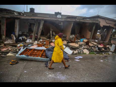 A woman walks in the rain past earthquake-destroyed homes the day after Tropical Storm Grace swept over Les Cayes, Haiti, Tuesday, August 17, 2021, three days after a 7.2-magnitude earthquake hit. 