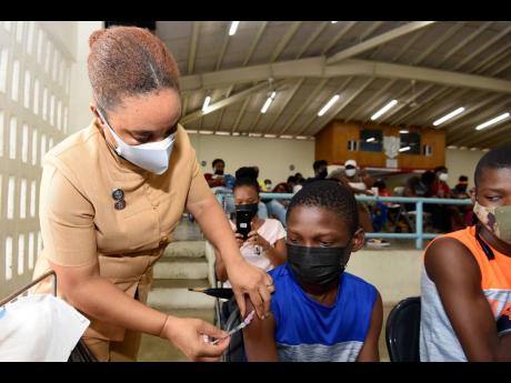 Public health nurse Shorna McGhie vaccinates Dejaun Folkes of Kingston College during a vaccination blitz at St George's College on Saturday.
