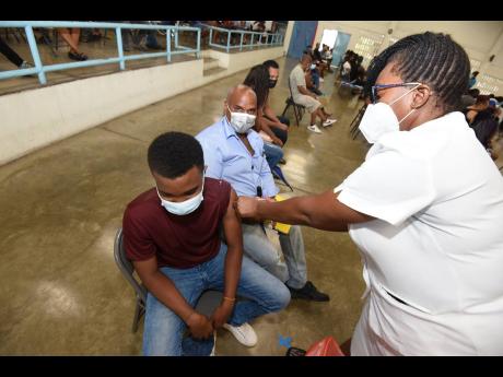 Ian Gray watches closely has registered midwife Ann-Marie Amos vaccinates his son, Matt, of Kingston College, during a vaccination blitz at St George’s College on Saturday.