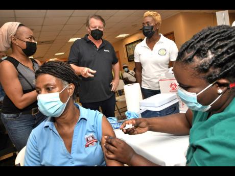 Nurse Jodian Walford (right) administers a dose of COVID-19 vaccine to J. Wray & Nephew employee Michille Buchanan at the company’s Spanish Town Road headquarters as part of a Private Sector Vaccination Initiative inoculation drive on Wednesday. In the b
