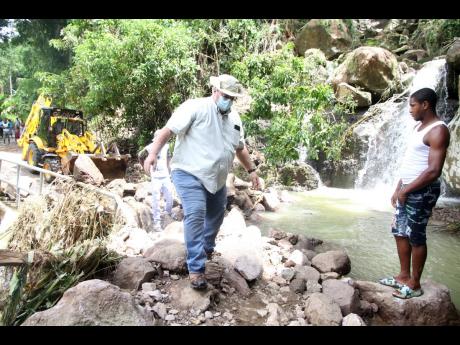 Phillip Henriques, member of parliament for Clarendon North Western, gingerly crosses a pathway blocked by a landslide near Devil’s Falls along the Thompson Town to Smithville main road on Saturday. 