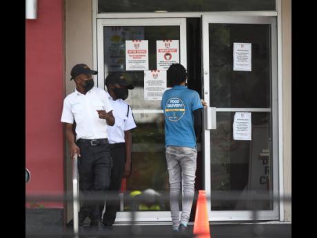 Security guards at the entrance to KFC’s Old Hope Road location look on as a 7Krave delivery man enters the restaurant. 