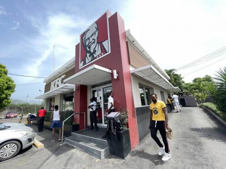 A customer waits in hope outside the entrance to KFC Old Hope Road as a delivery man walks from the drive-through window on Sunday.