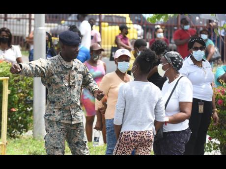 A soldier speaks with some of the hundreds of persons who turned out at the National Arena in Kingston yesterday to be vaccinated against COVID-19. Many persons stated that they chose Monday to take the vaccine because it was a no-movement day and would be