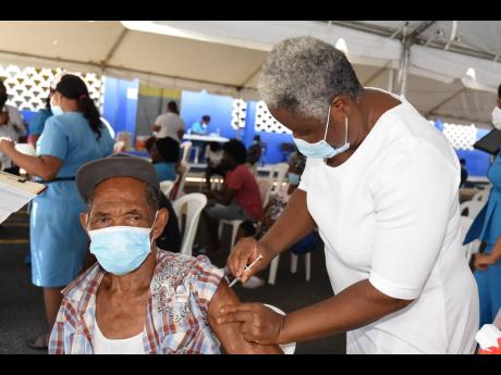 Registered nurse Ann Ikeche administers a dose of COVID-19 vaccine to Sam Williams at Jones Town Primary on Thursday. This was part of a vaccination exercise at two sites in the St Andrew Southern constituency. 