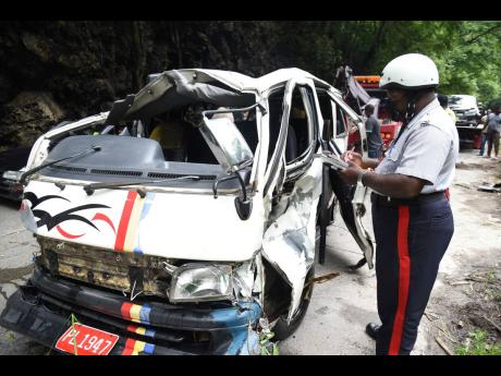 Police corporal Everton Allen jots down notes while observing the mangled Toyota Hiace minibus that had plunged into the Rio Cobre after colliding with a Toyota Fielder station wagon on Tuesday. Valerie Ennis, 59, died from crash-related injuries. 