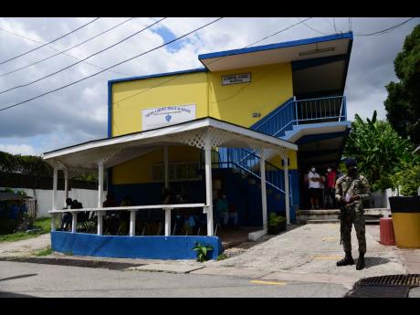 A soldier stands guard near the Curtis Cole Building at Merl Grove High School in St Andrew during a vaccination blitz on Sunday. The school’s administration has been thrown into turmoil after principal Dr Marjorie Fullerton was suspended by the board.