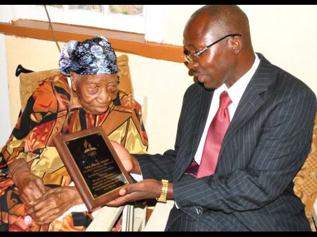 Pastor Carlington Hylton, community services director of the North Jamaica Conference of Seventh-day Adventists, presents a plaque to Violet Moss Brown, Jamaica’s oldest woman, to mark her 115 birthday in 2015.