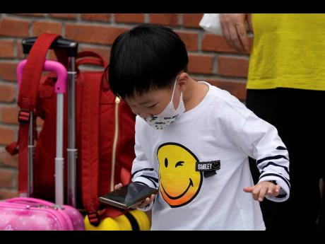 AP
A child wearing a face mask plays game on a smartphone next to his relative in Beijing Sept. 12, 2021. 