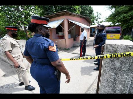 Inspector N. Brown (left) and other police gather at the house where Sergeant Averel McCollin was shot by gunmen in Gregory Park, Portmore, on Sunday. McCollin died while undergoing surgery at the Spanish Town Hospital. 