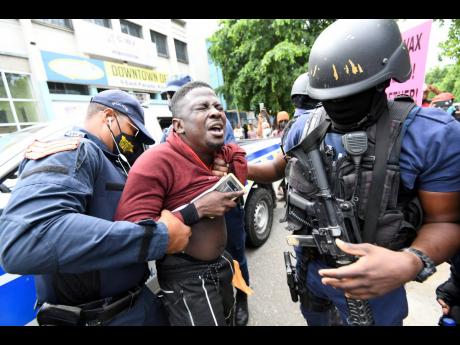Police officers search one of the protesters before detaining him as they tried to break up an unauthorised march against COVID-19 vaccines in downtown Kingston yesterday.