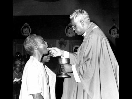 President Julius K. Nyerere of the United Republic of Tanzania (left) taking a holy Communion from the Roman Catholic Archbishop of Kingston, the Most Rev Samuel Carter, at the Holy Trinity Cathedral. Madame Nyerere, kneeling beside her husband, also took 