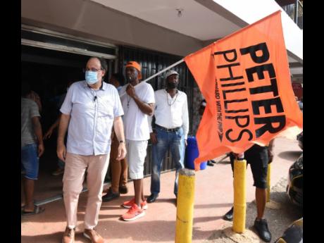 A Peter Phillips loyalist waves a flag honouring the former party leader as PNP President Mark Golding meets and greets supporters in Royal Flat, Manchester, during a tour. 