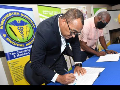 Dr Christopher Tufton, minister of health and wellness, inks an agreement with Dr Orville Nembhard, director of Health Plus Associates, during a ceremony involving 11 private-sector partners who the ministry will engage to administer COVID-19 vaccines. The