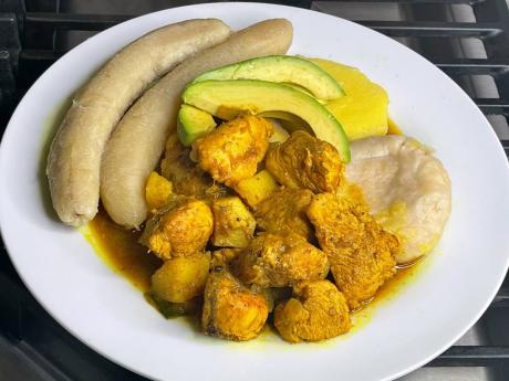 Curried chicken, paired with boiled green bananas and a dumpling, served with slices of avocado.