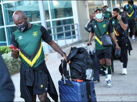 National senior men’s footballer Javon East (front) checks his phone upon arrival at the Norman Manley International Airport in Kingston on Friday evening, ahead of the Reggae Boyz’s FIFA World Cup qualifying match against Canada on Sunday. Also pictur