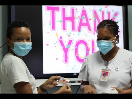 Angella Byfield (left), a member of the Preemie Foundation of Jamaica, gives an ID pin to Nurse Shelly Latchman as she collects her lunch during the treat.