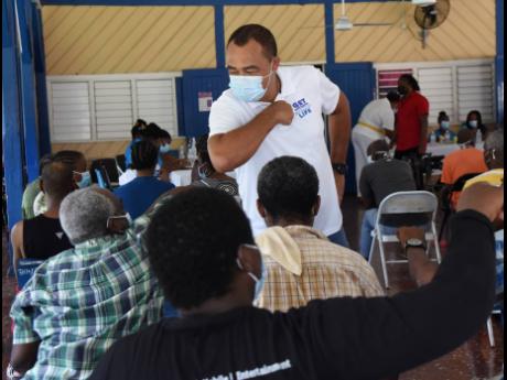 Health and Wellness Minister Dr Christopher Tufton (standing) greets patients at the Bellevue Hospital in Kingston during a vaccination drive at the mental health institution yesterday.