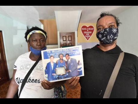 Sandra Brown (left) and Simone Henry, residents of Standpipe in St Andrew, hold a photo of Dr Lloyd Cole making a presentation to Brown’s daughter, Tamara Reid. Former US Ambassador Sue Cobb is at left in the photo. 