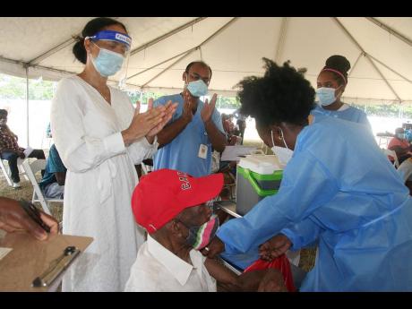 Caron Chung (left), executive director of The American Friends of Jamaica (AFJ), and Dr Kaushal Singh (second left), medical officer of health for Hanover, applaud 101-year-old Terrence James (seated) as he receives his vaccination against the COVID-19 vir