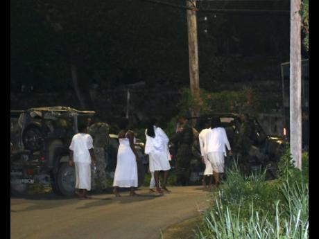 
Under the watchful eyes of Jamaica Defence Force personnel, members of the Pathways International Kingdom Restoration Ministries make their way to a service vehicle to be taken away for questioning after last Sunday’s deadly ritual.