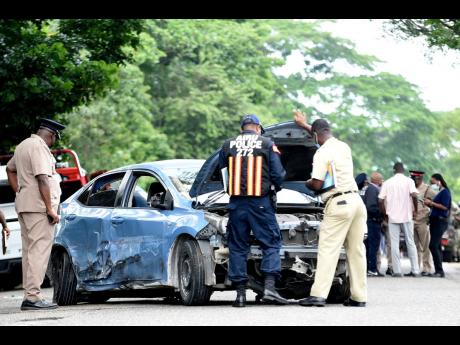 Policemen look under the bonnet of the death car in which Kevin O. Smith and Constable Orlando Irons were travelling. Smith and Irons died on Monday, while two other policemen were hospitalised with serious injuries.