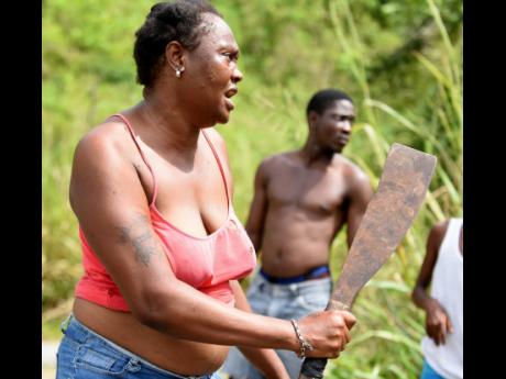 A woman armed with a machete participates in the manhunt for Davian Bryan, the alleged abductor of two children in Bath, St Thomas. The children were rescued but Bryan is still at large.